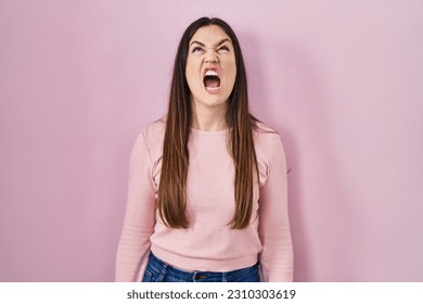 Young brunette woman standing over pink background angry and mad screaming frustrated and furious, shouting with anger. rage and aggressive concept.  - Shutterstock ID 2310303619