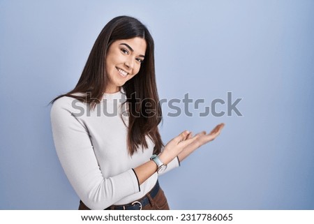 Young brunette woman standing over blue background inviting to enter smiling natural with open hand  Foto stock © 