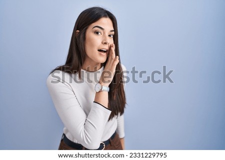 Young brunette woman standing over blue background hand on mouth telling secret rumor, whispering malicious talk conversation 