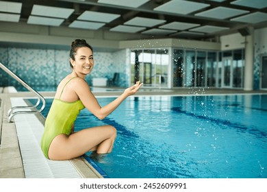 A young brunette woman in a swimsuit sitting on the edge of an indoor swimming pool, finding peace and serenity. - Powered by Shutterstock