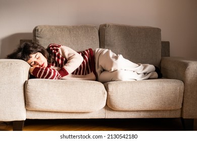 A young brunette woman takes a siesta on her grey sofa in her living room at home