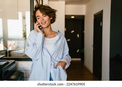 Young brunette woman talking on mobile phone while standing in modern office - Shutterstock ID 2247619905
