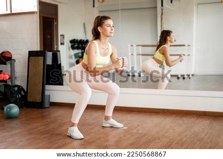 Young brunette woman with a toned body doing squats . Women's tight sportswear.