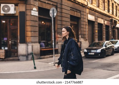 Young brunette woman walking on the street wear navy blue bomber jacket. Portrait of a young woman depressed and lonely walk outdoors.