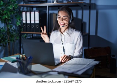 Young Brunette Woman Wearing Call Center Agent Headset Working Late At Night Showing And Pointing Up With Fingers Number Two While Smiling Confident And Happy. 