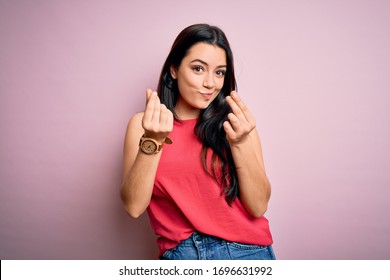 Young Brunette Woman Wearing Casual Summer Shirt Over Pink Isolated Background Doing Money Gesture With Hands, Asking For Salary Payment, Millionaire Business