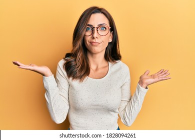 Young brunette woman wearing casual clothes and glasses clueless and confused with open arms, no idea and doubtful face. 