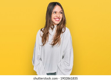 Young brunette woman wearing casual turtleneck sweater looking away to side with smile on face, natural expression. laughing confident. 