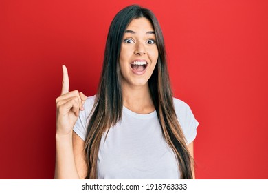 Young Brunette Woman Wearing Casual White Tshirt Over Red Background Pointing Finger Up With Successful Idea. Exited And Happy. Number One. 