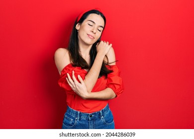 Young brunette woman wearing casual red shirt hugging oneself happy and positive, smiling confident. self love and self care 