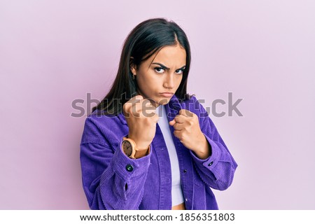 Young brunette woman wearing casual clothes ready to fight with fist defense gesture, angry and upset face, afraid of problem 