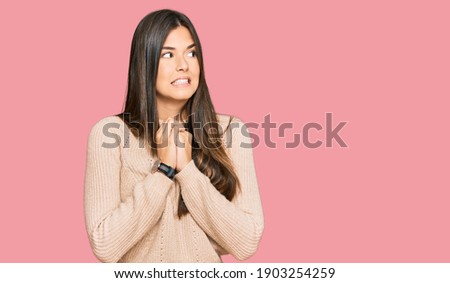 Young brunette woman wearing casual winter sweater laughing nervous and excited with hands on chin looking to the side 
