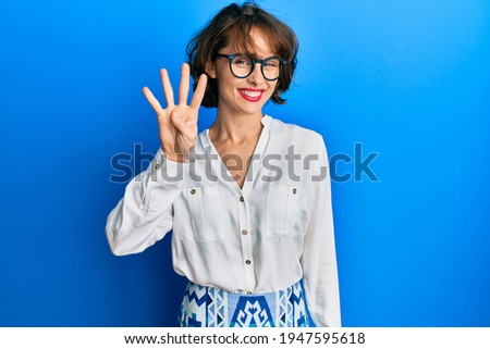 Young brunette woman wearing casual clothes and glasses showing and pointing up with fingers number four while smiling confident and happy. 