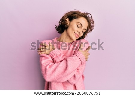 Young brunette woman wearing casual winter sweater hugging oneself happy and positive, smiling confident. self love and self care 