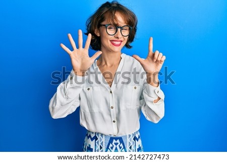 Young brunette woman wearing casual clothes and glasses showing and pointing up with fingers number seven while smiling confident and happy. 