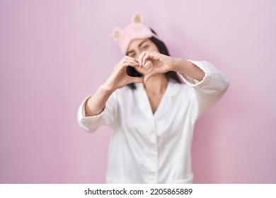 Young brunette woman wearing sleep mask and pajama smiling in love showing heart symbol and shape with hands. romantic concept.  - Shutterstock ID 2205865889