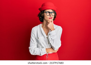 Young Brunette Woman Wearing Stewardess Style And Glasses Serious Face Thinking About Question With Hand On Chin, Thoughtful About Confusing Idea 