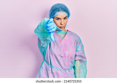 Young Brunette Woman Wearing Surgeon Uniform And Medical Mask Looking Unhappy And Angry Showing Rejection And Negative With Thumbs Down Gesture. Bad Expression. 