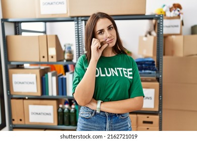 Young brunette woman wearing volunteer t shirt at donations stand mouth and lips shut as zip with fingers. secret and silent, taboo talking 