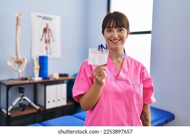 Young brunette woman working at rehabilitation clinic showing id looking positive and happy standing and smiling with a confident smile showing teeth  - Shutterstock ID 2253897657
