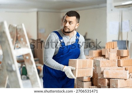 Young builder working on a construction site indoors is laying bricks on top of each other
