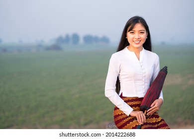 A young Burmese woman is walking with a red umbrella on U-bein bridge, Mandalay, Myanmar. Space for text. - Shutterstock ID 2014222688