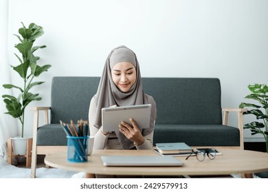 Young business Asian Business muslim woman in hijab using a tablet, Sitting near the window in the living room.  - Powered by Shutterstock