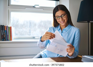 Young Business Entrepreneur Checking Her Mail Sitting At Her Desk At Home With An Open Letter In Her Hand