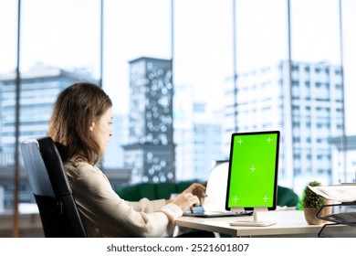 Young business entrepreneur looking at green screen mockup on her gadgets, working in modern urban corporate office. Female leader developing a strategy to increase funding for success. - Powered by Shutterstock