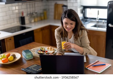 Mujer joven empresaria que trabaja en casa mientras desayuna. Usando un ordenador portátil en la cocina. Trabajando en línea.