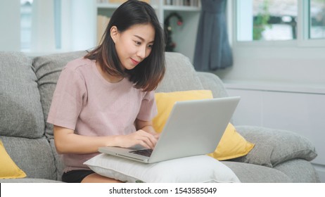 Young business freelance Asian woman working on laptop checking social media while lying on the sofa when relax in living room at home. Lifestyle latin and hispanic ethnicity women at house concept.