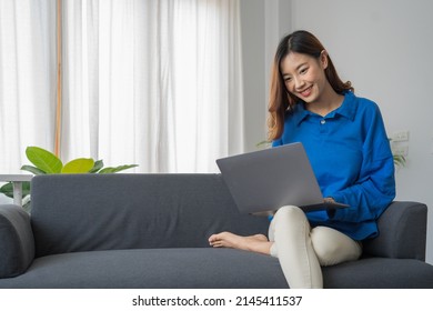 Young Business Freelance Asian Woman Working On Laptop Checking Social Media While Sitting On The Sofa When Relax In Living Room At Home.