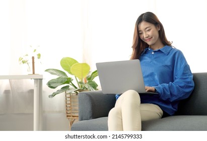 Young Business Freelance Asian Woman Working On Laptop Checking Social Media While Lying On The Sofa When Relax In Living Room At Home.