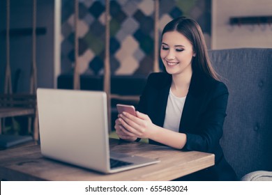 Young business lady is smiling because of lovely sms on her phone in the cafe. She is wearing black jacket and white tshirt. Interior of cafe is very modern