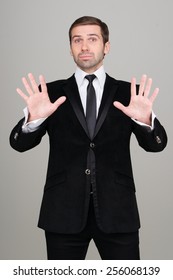 Young Business Man In Black Suit Making Calm Down Gesture. Studio Portrait. Easy. Relax.