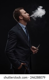 Young Business Man Blowing Smoke Of Electronic Cigarette On Dark Background