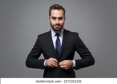 Young business man in classic black suit shirt tie posing isolated on grey wall background studio portrait. Achievement career wealth business concept. Mock up copy space. Fastening button on jacket