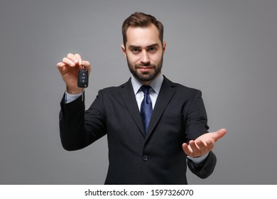 Young Business Man In Classic Black Suit Shirt Tie Posing Isolated On Grey Background. Achievement Career Wealth Business Concept. Mock Up Copy Space. Standing With Otstretched Hand, Holding Car Keys