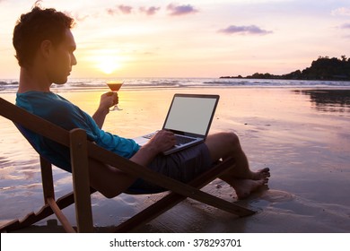 Young Business Man With Cocktail Working On Laptop On The Beach At Sunset, Freelance Job Online, Focus On The Screen