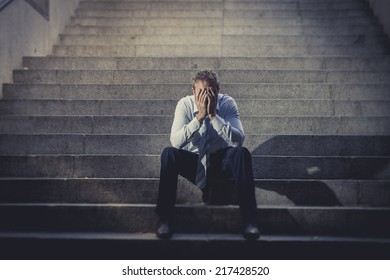 Young Business Man Crying Abandoned Lost In Depression Sitting On Ground Street Concrete Stairs Suffering Emotional Pain, Sadness, Looking Sick In Grunge Lighting