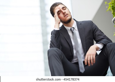 Young Business Man Crying Abandoned Lost In Depression Sitting On Ground Street Concrete Stairs Suffering Emotional Pain, Sadness, Looking Sick In Grunge Lighting