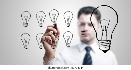 Young Business Man Drawing Many Small Light Bulbs Equal A Big One. Man Coming Up With An Idea On A Glass Screen With Black Marker. On A Gray Background