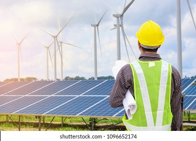 Young business man engineer with yellow helmet at solar panel and wind generators power plant construction site background