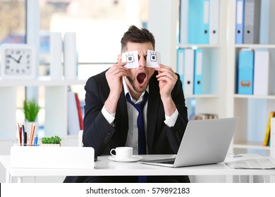 Young business man with fake eyes painted on paper stickers yawning at workplace in office - Powered by Shutterstock