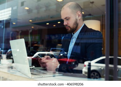 Young Business Man Leadership Of Big Successful Enterprise Is Checking The Status Of Bank Account Via App On Mobile Phone After Make On-line Purchases Via Laptop Computer. Work Break In Coffee House