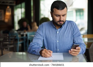 Young business man looking on phone and writing on paper - Shutterstock ID 744184651