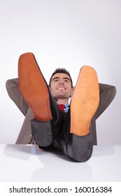 young business man looking upward, away from the camera while holding his hands behind his head and his feet on the desk. on a gray background