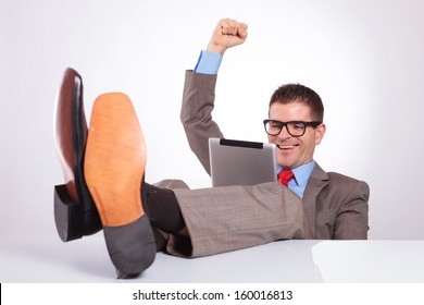 young business man reading something on his tablet and cheering while holding his feet on his desk. on a gray background