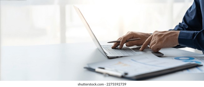 young business man Recording data on laptop, comparing details from graphs. Business income charts in the areas of real estate, tax, management, technology marketing in a private office. - Powered by Shutterstock