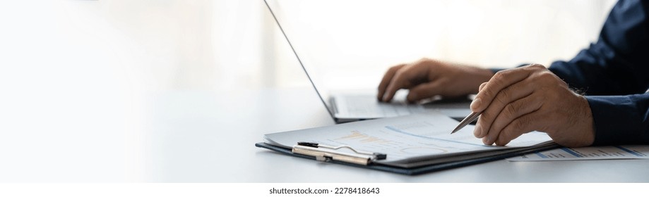 young business man Recording data on laptop, comparing details from graphs. Business income charts in the areas of real estate, tax, management, technology marketing in a private office. - Shutterstock ID 2278418643